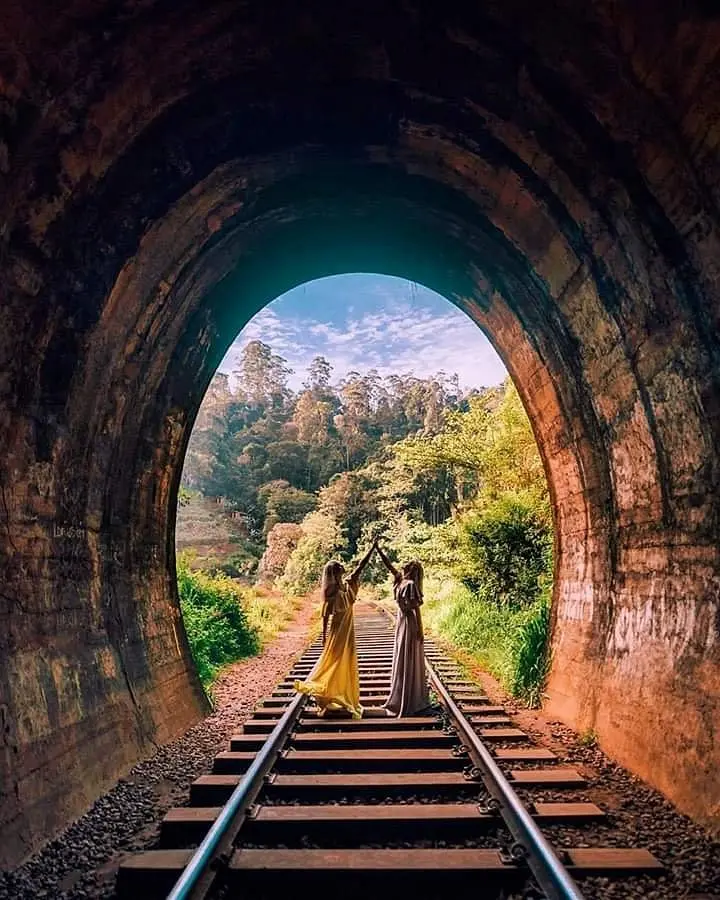 A colonial-era steam train exiting the dark, curved Demodara tunnel into the bright sunlight of the hill country.